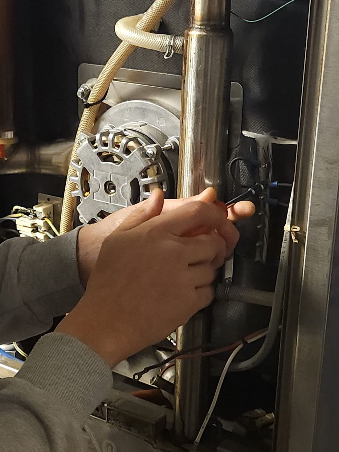 Hände prüfen die Anschlüsse am Lüftermotor eines Gastrogeräts